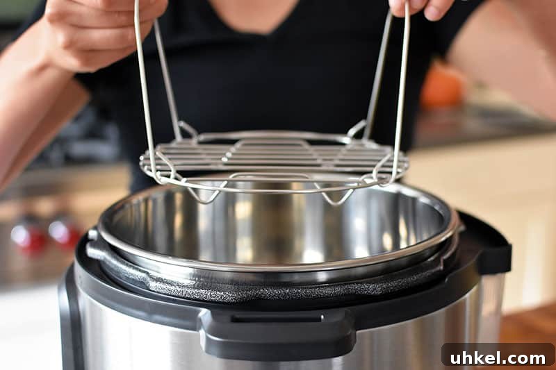 Instant Pot Spaghetti Squash — Quick Foolproof Pressure Cooker Recipe 9 A closeup of two hands lowering a stainless steel steaming rack into an open Instant Pot.