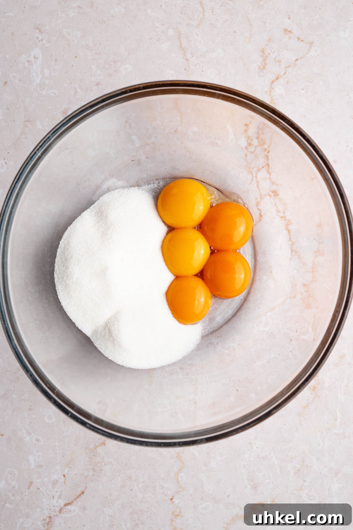 Egg yolks in a glass bowl with sugar before mixing.