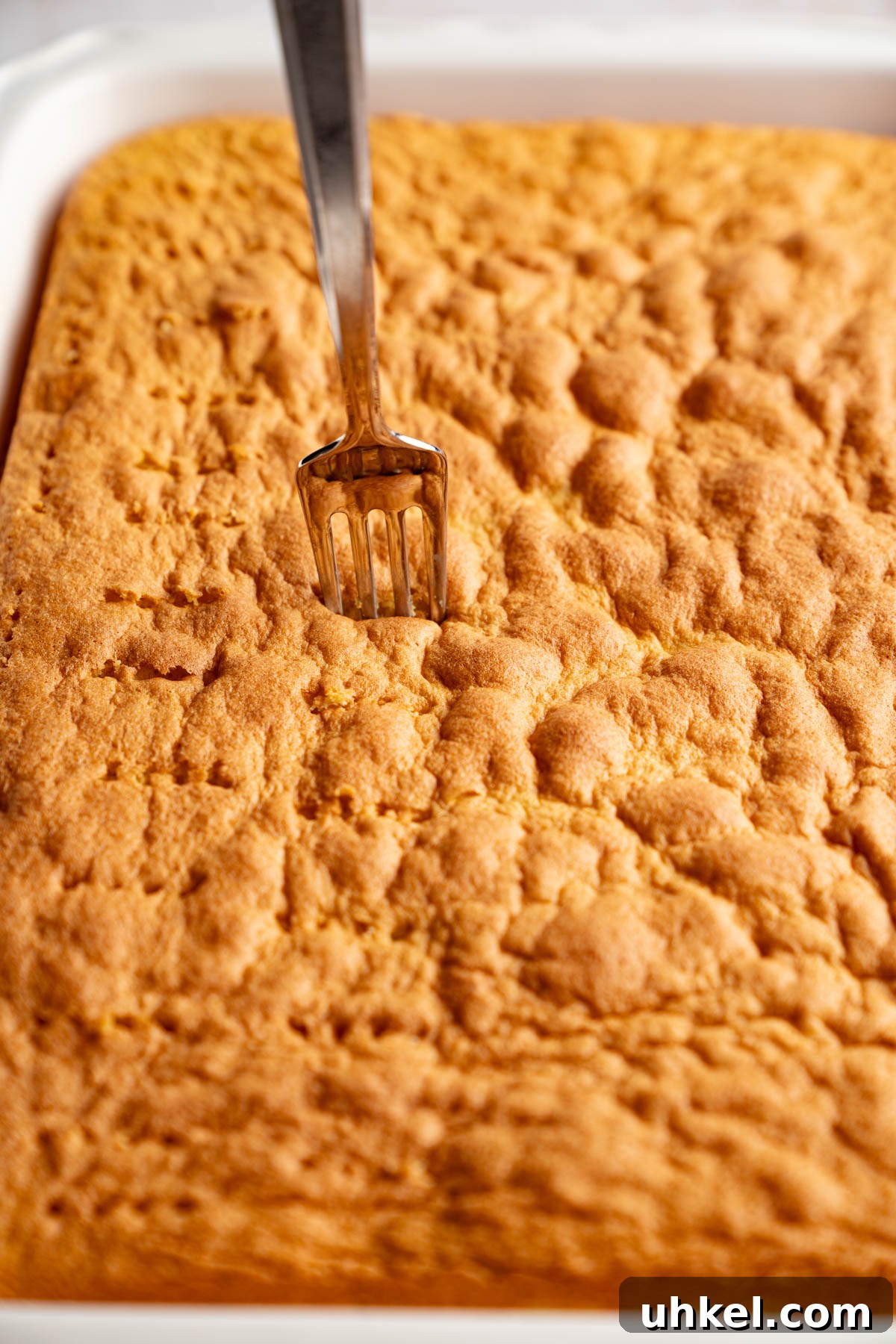 A fork poking holes in the baked cake.