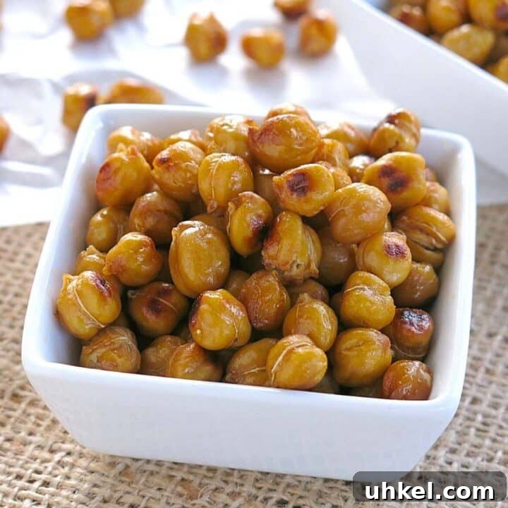 Roasted buffalo chickpeas in a square white bowl with more on parchment paper behind it.