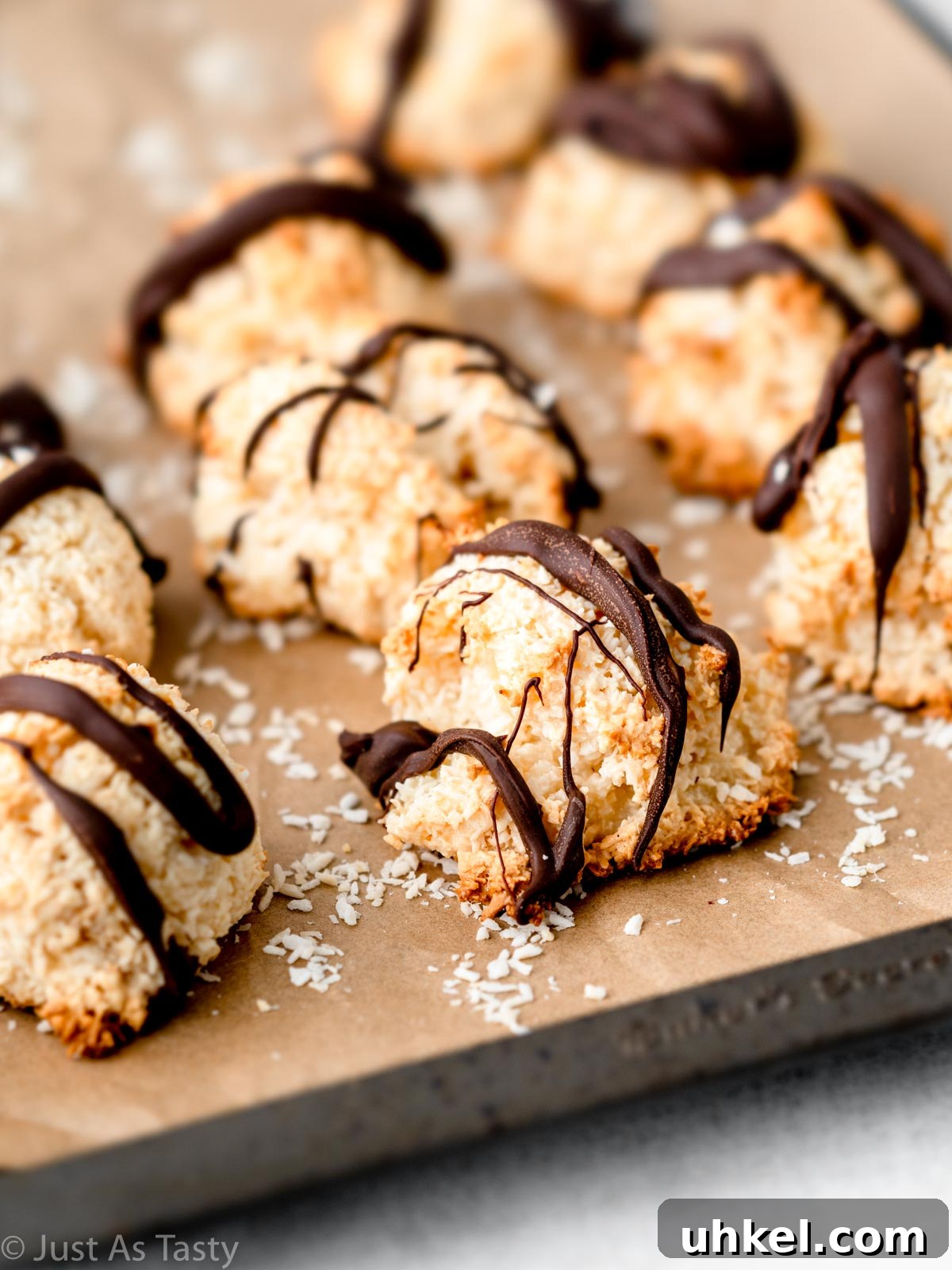 Chewy Chocolate Coconut Macaroons Made with Condensed Milk 7 Coconut macaroons drizzled with chocolate on a lined baking sheet.