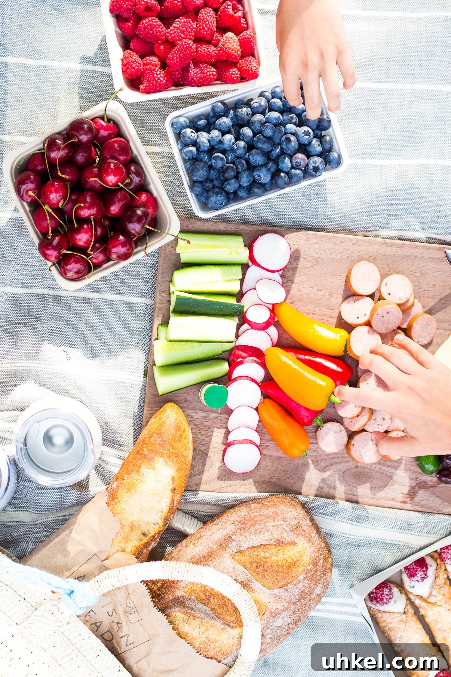 Overhead shot of picnic food on a blanket with two hands reaching in