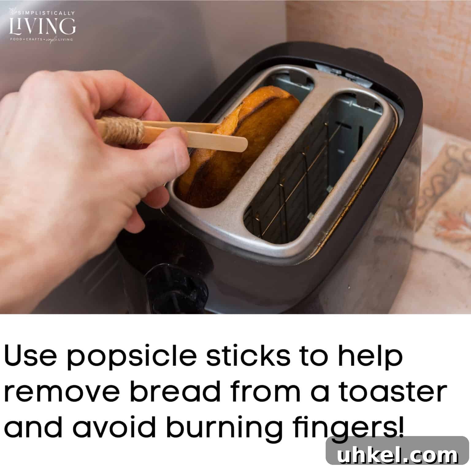 a hand using popsicle sticks to remove a piece of bread from toaster