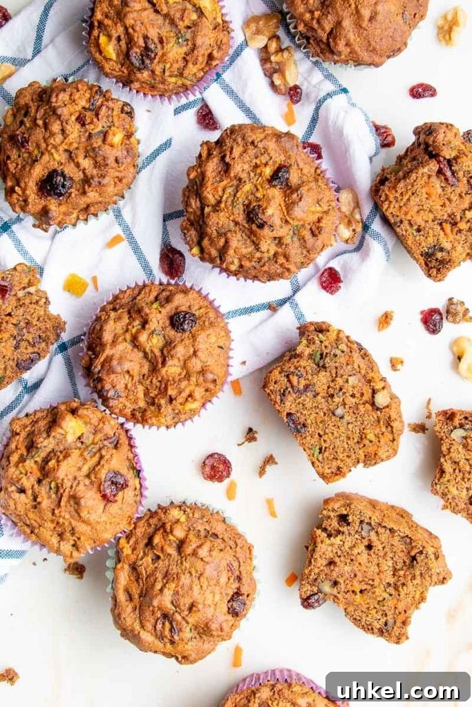 Morning Glory Muffins with Carrots, Apples & Nuts 10 A bunch of muffins scattered on a tea towel with blue wide plaid. some muffins are cut open to see the insides, with walnuts, shredded carrots and zucchini plus dried cranberries.