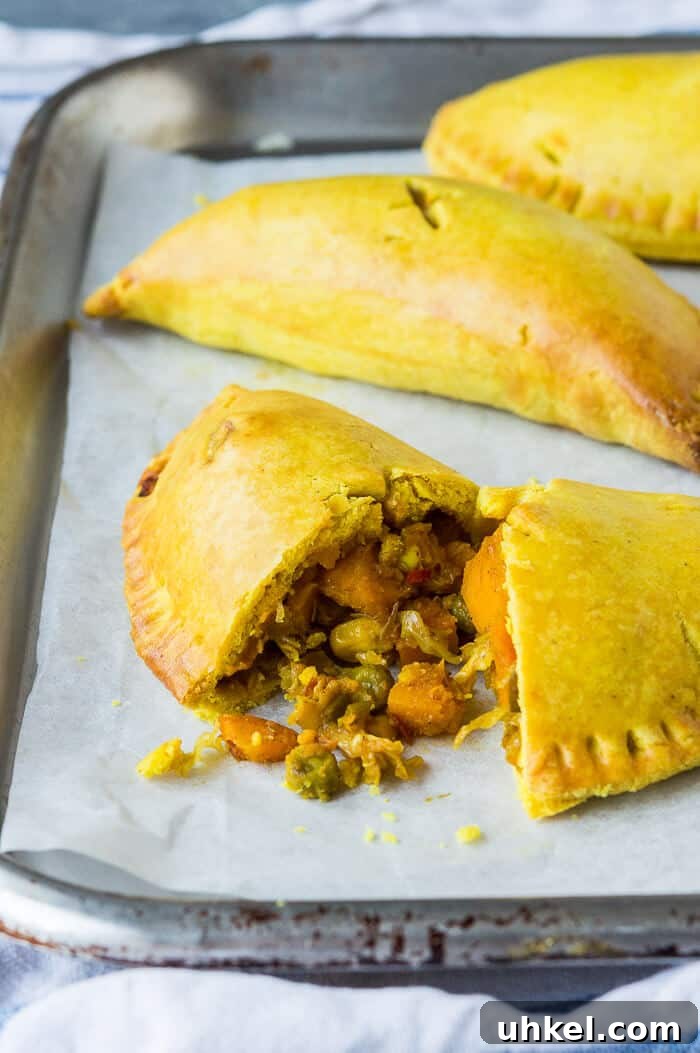 Jamaican vegetable patties - these spiced, Caribbean style vegan vegetable pasties are full of flavour and make a great snack or light meal. Eggless and dairy-free. #veganmeals #veganbaking #meatfree #plantbased Close up a vegan Jamaican vegetable patty sliced in half.