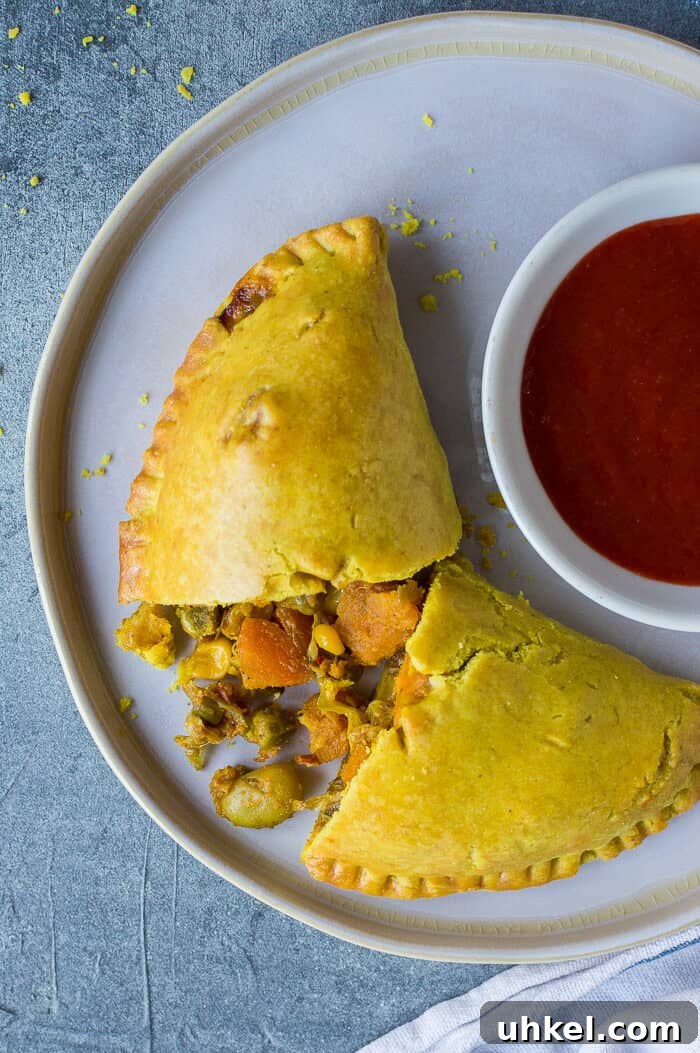 Vegan Jamaican Vegetable Patties: Flaky Caribbean Empanadas 6 A Jamaican vegetable patty on a white plate with a bowl of hot sauce.