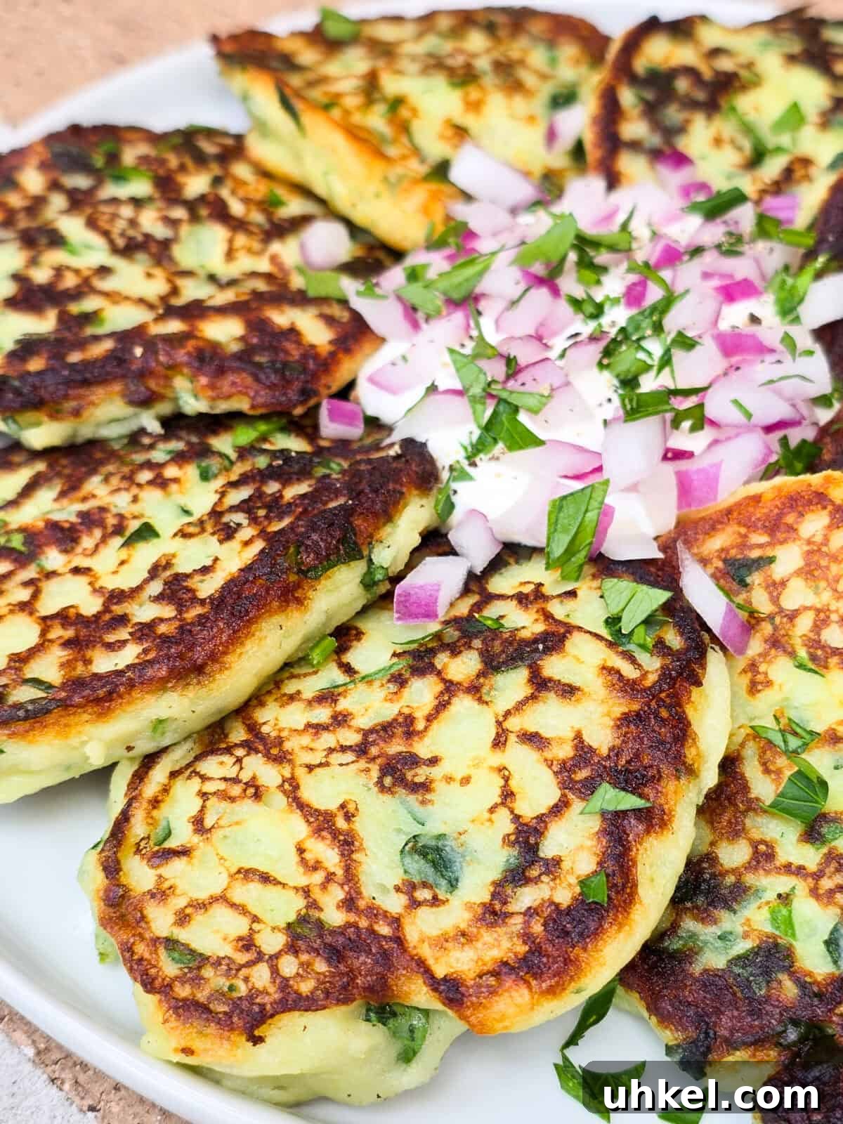 Crispy Garlic and Spinach Mashed Potato Cakes 3 prepared instant mashed potato cakes on plate with sour cream and red onion in the center