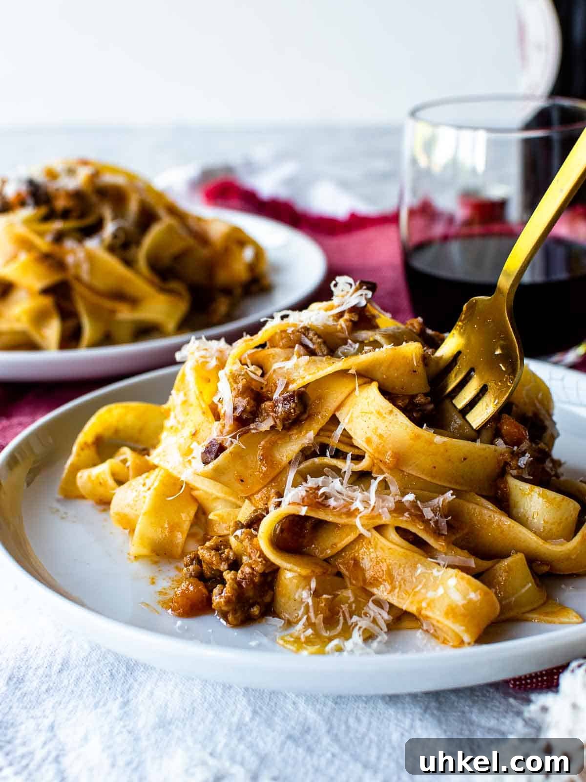Authentic Tagliatelle alla Bolognese Recipe 2 White plate with tagliatelle alla bolognese pasta on it and a gold fork in the pasta.