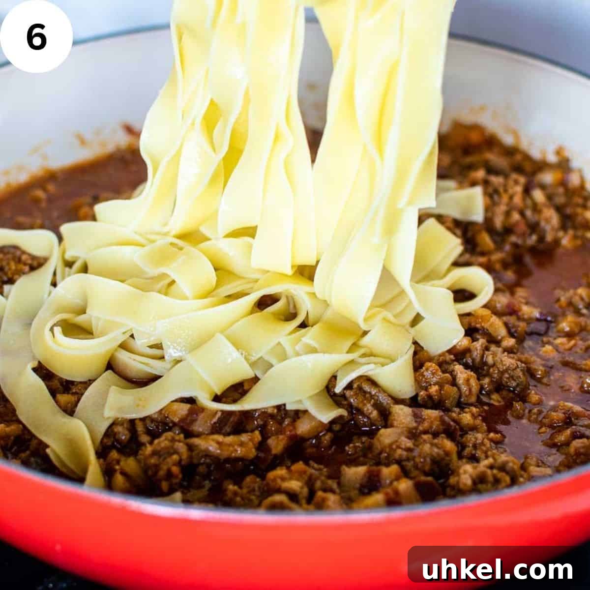 Authentic Tagliatelle alla Bolognese Recipe 9 Tagliatelle being added to meat sauce in a round pan.