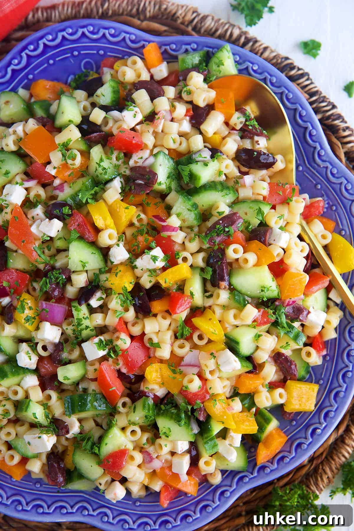 Greek Pasta Salad with Feta, Olives & Fresh Tomatoes 6 Greek Pasta Salad on a blue platter with a gold serving spoon in it.