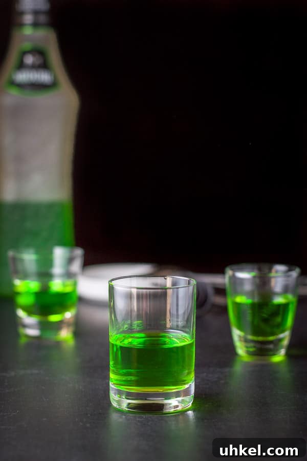 Mangled Frog Shot: 12 Christmas Shot Recipes 5 Midori poured into the glasses with the bottle in the background