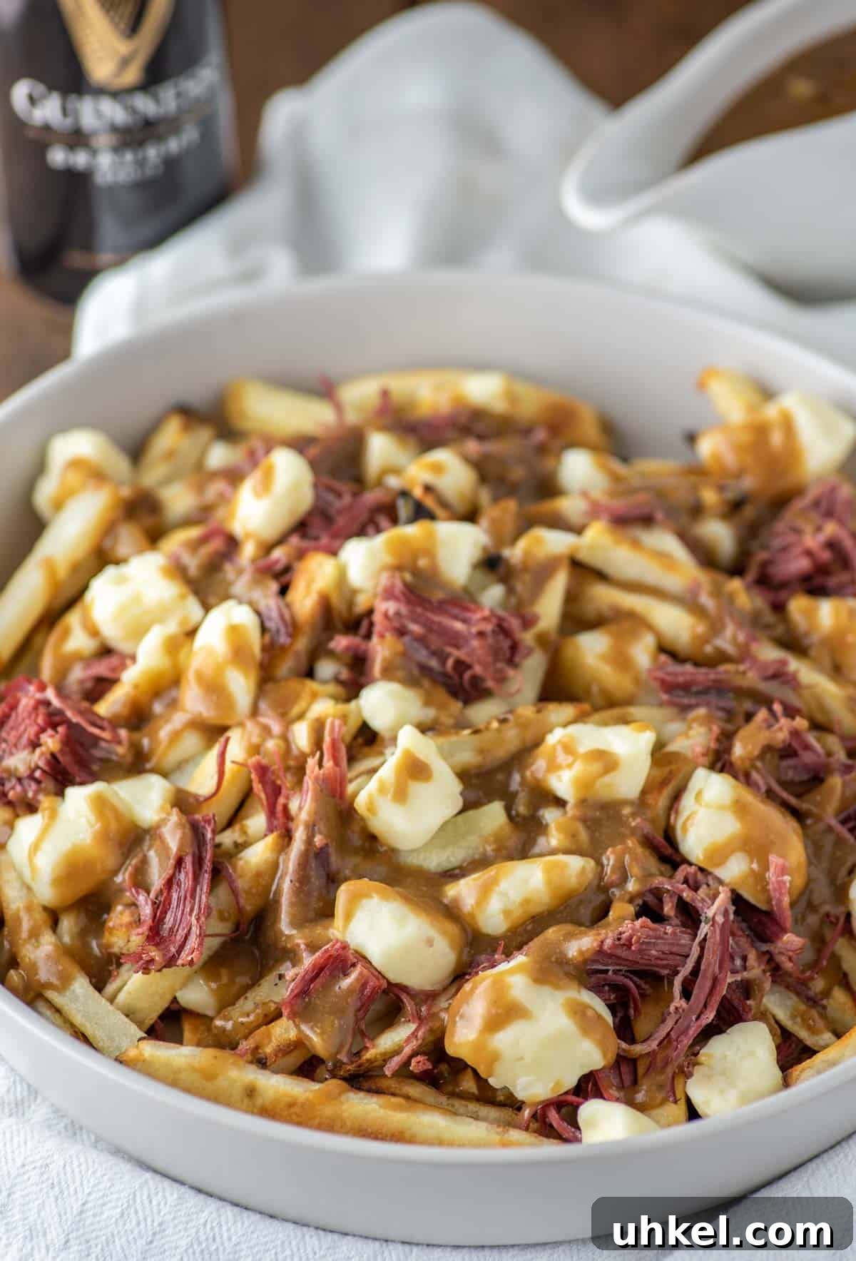 Corned Beef Poutine Topped with Guinness Gravy 2 corned beef poutine in bowl with gravy and Guinness in background