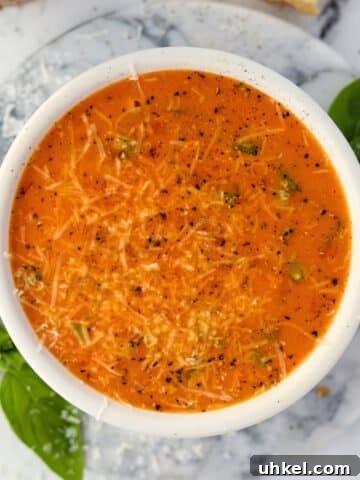 A bowl of cherry tomato soup garnished with parmesan cheese, basil, and cracked black pepper.
