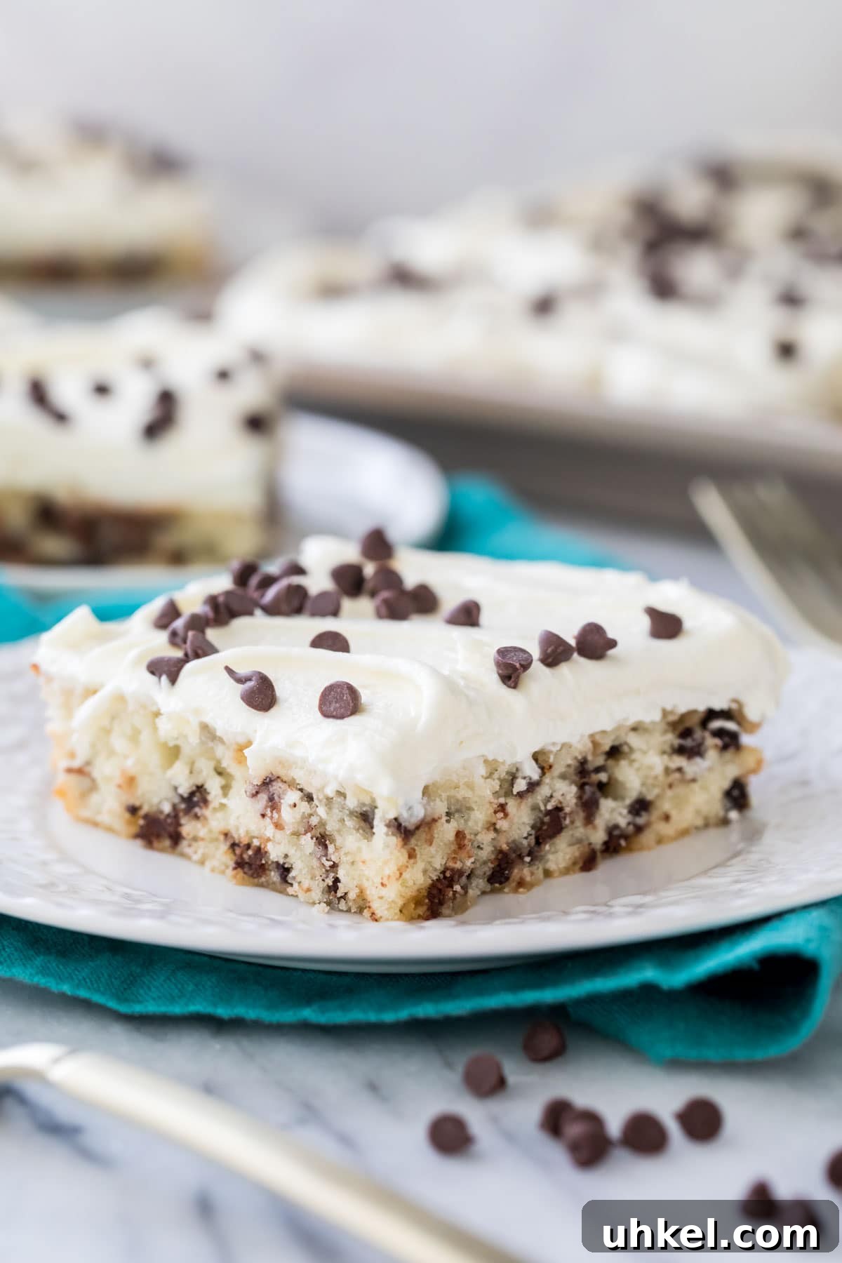 Classic Chocolate Chip Sheet Cake Recipe 2 Square slice of chocolate chip sheet cake on a white plate. Frosted with white frosting and mini chocolate chips
