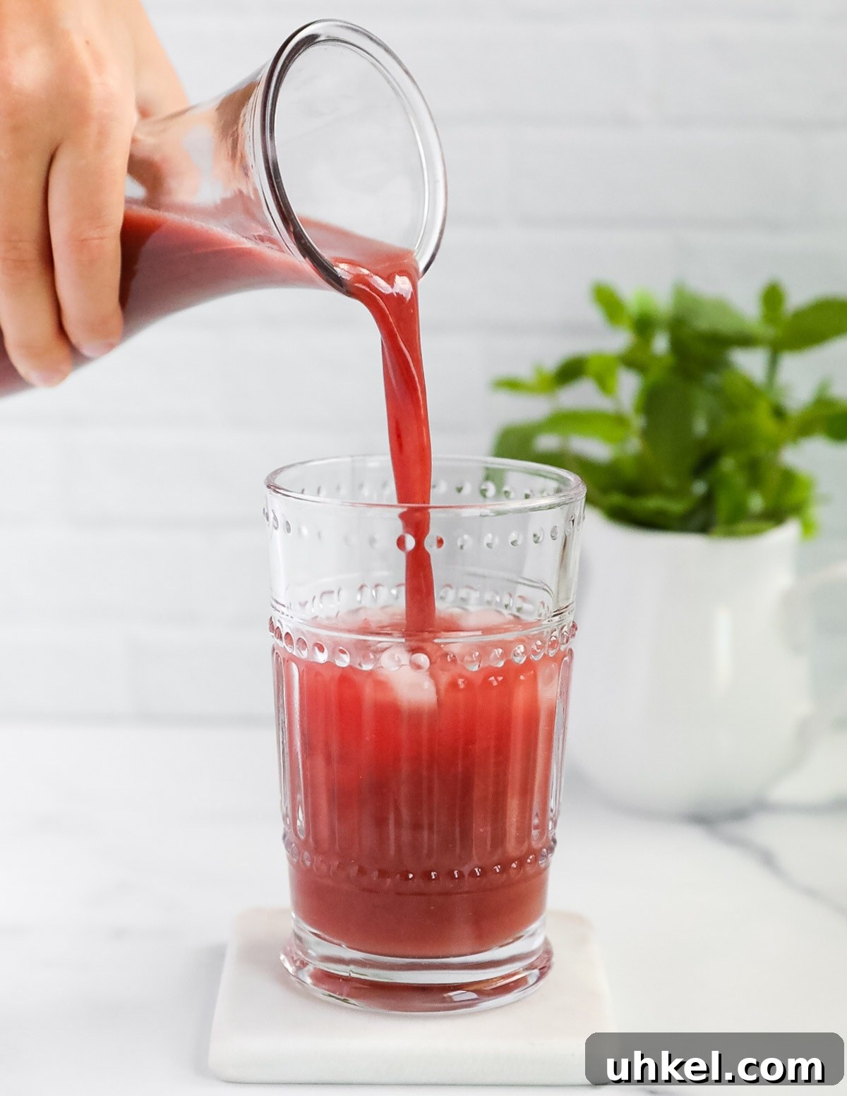 Homemade Strawberry Acai Lemonade 5 A hand pouring a pitched of bright pink lemonade into a clear glass