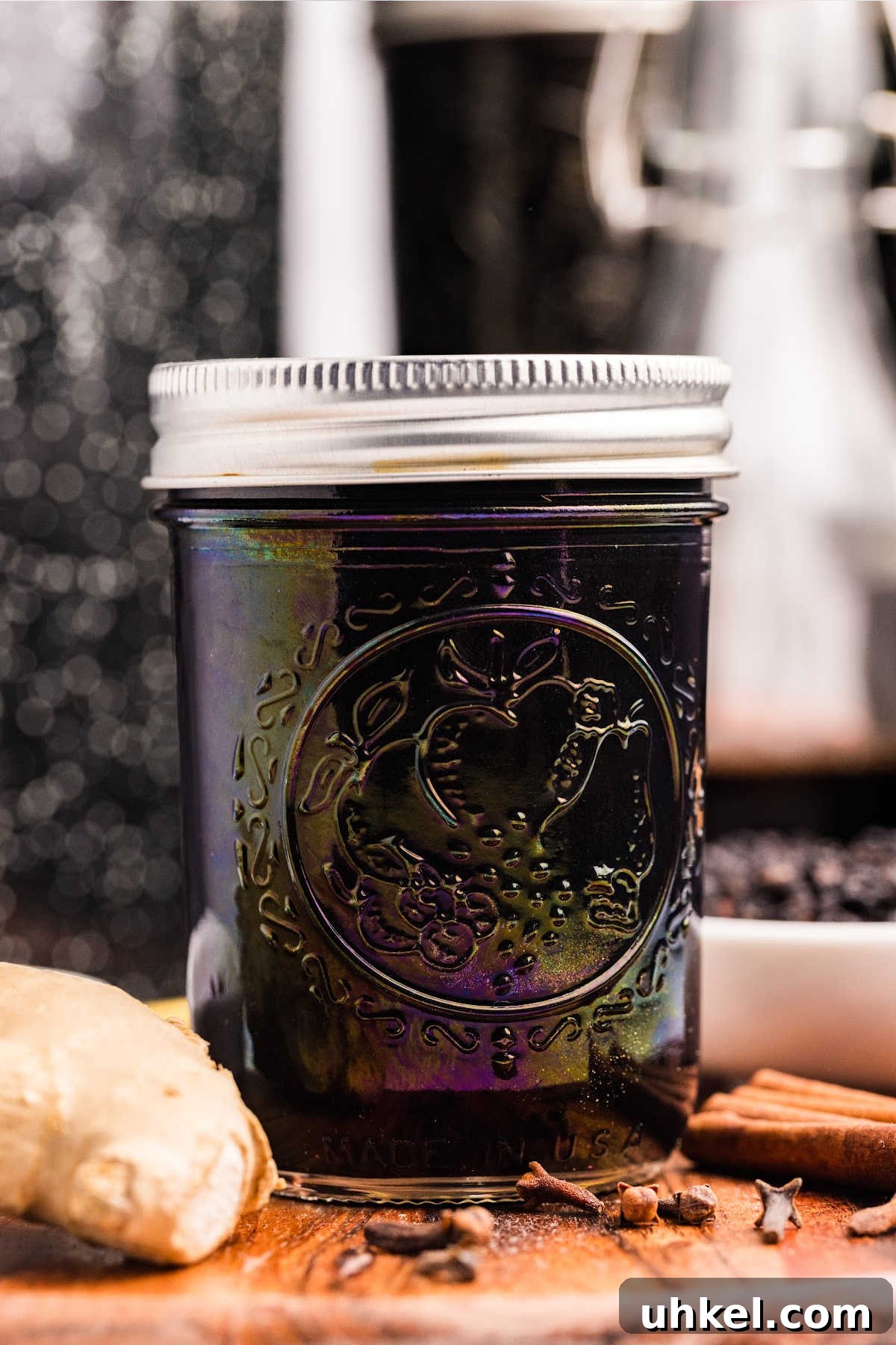 Spiced Elderberry Syrup: Step-by-Step Canning Instructions 2 sealed jar of elderberry syrup with piece of ginger and spices in front.
