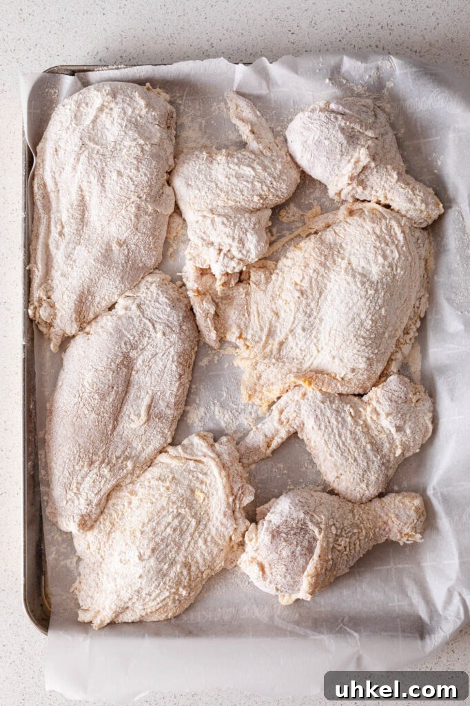Crispy Fried Chicken Without Buttermilk 9 flour coated chicken pieces on a parchment lined sheet pan
