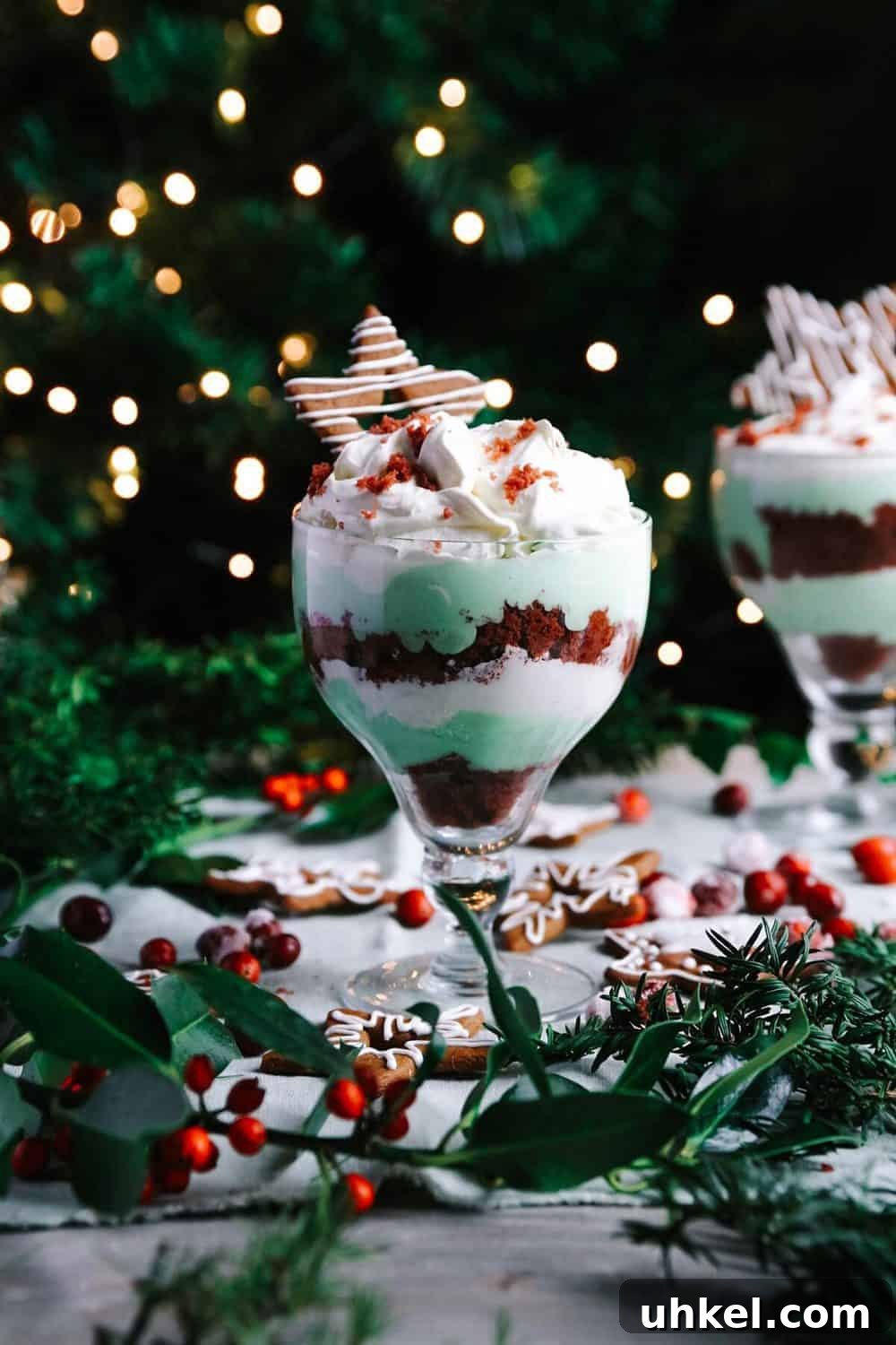Easy Christmas Trifle Glass dessert trifle with red velvet cake, green pudding, and whipped cream; Christmas decorations in background